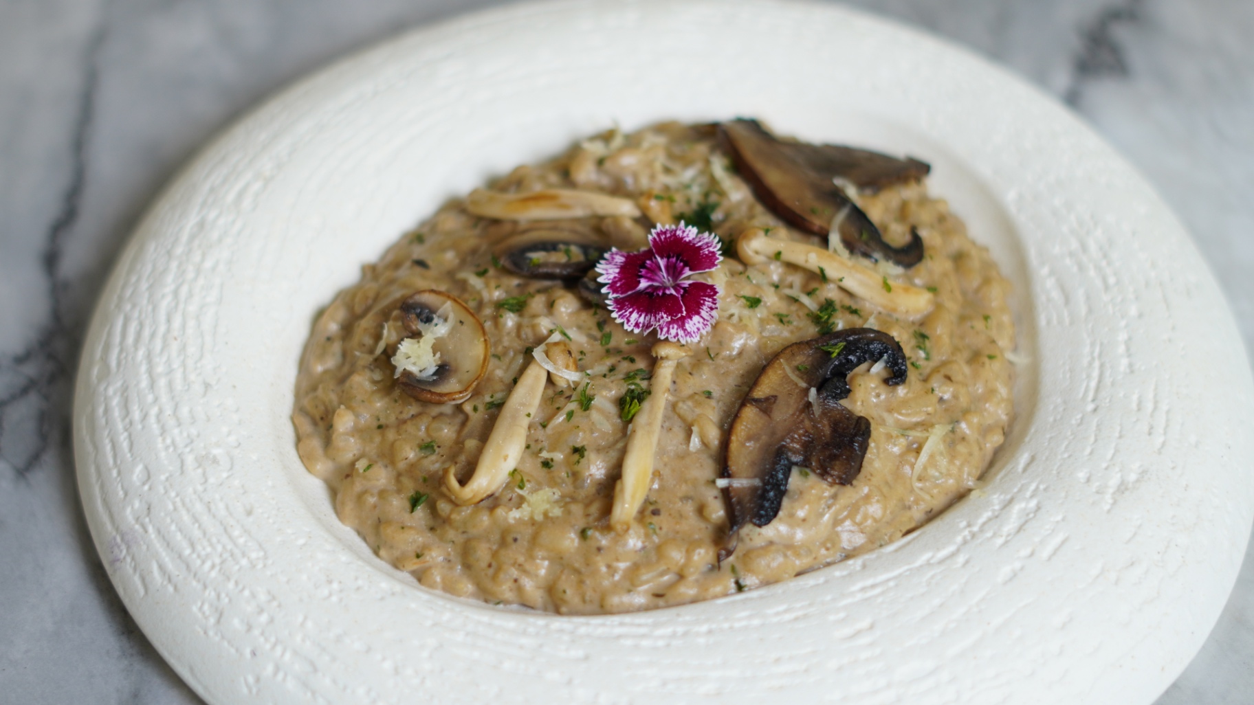 Creamy wild mushroom risotto topped with mushrooms and an edible flower