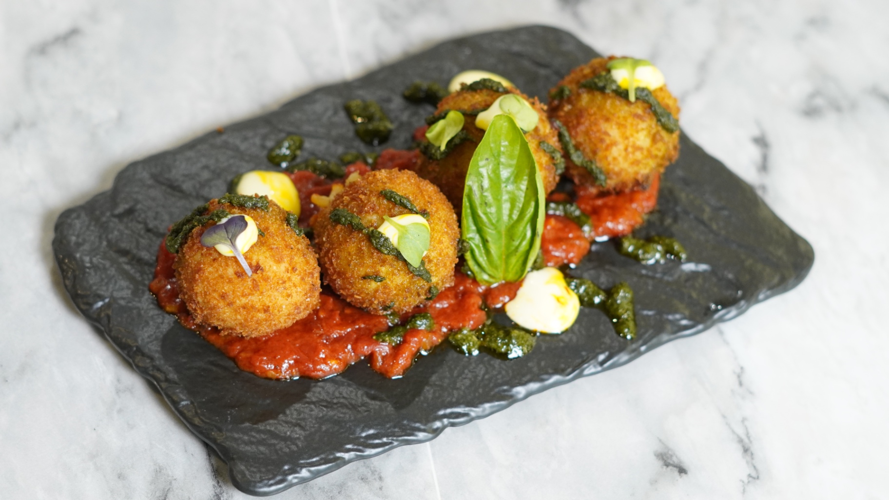 Saffron arancini balls on tomato sauce with basil and pesto